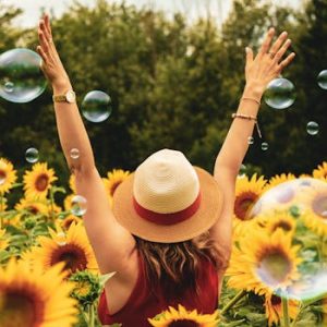 A joyful woman in a sunflower field with bubbles, expressing happiness on a summer day.